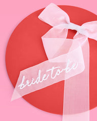 xo-fetti embroidery-script detail on white bow adds bridal flair for photos and events.