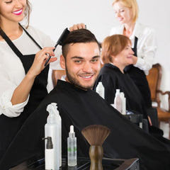 ProSuites barber cape on client, anti-static fabric protects clothing during haircut.