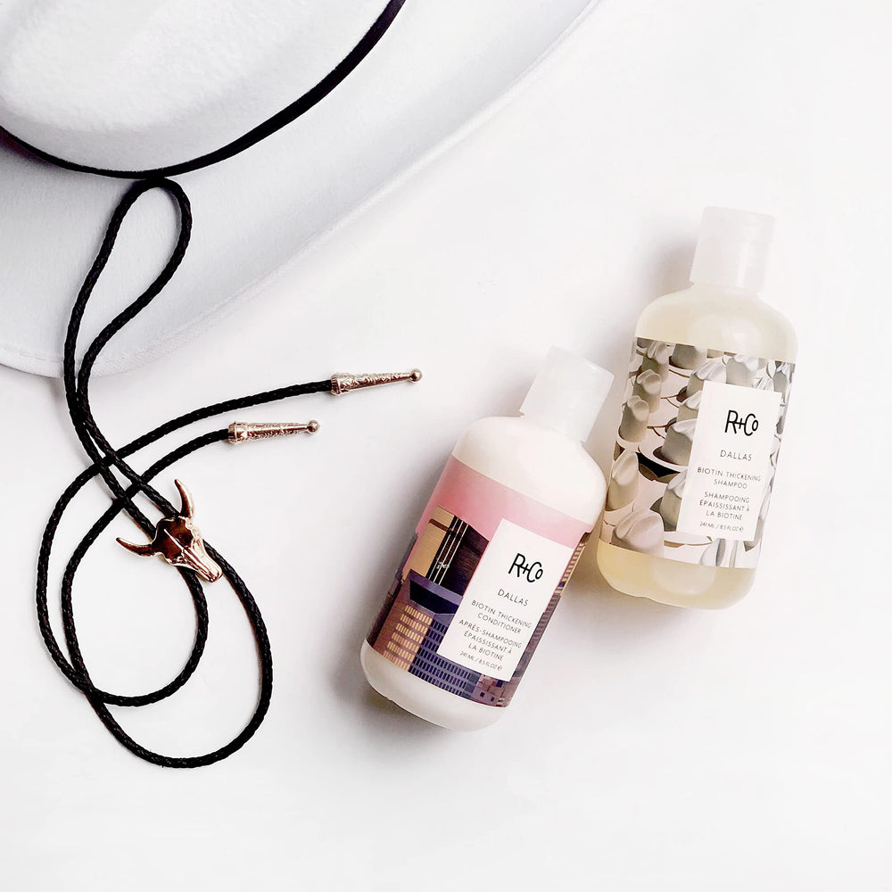 R+Co Dallas Thickening Shampoo amber bottle displayed on shelf.