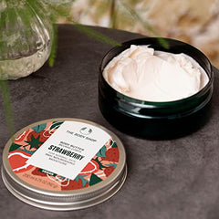 Hands applying The Body Shop Strawberry Body Butter for smooth, nourished skin.